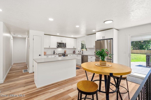 320 E Dakota Ave, Hayden, ID 83835 - kitchen featuring stainless steel appliances, light wood-type flooring, white cabinets, decorative backsplash, and a center island