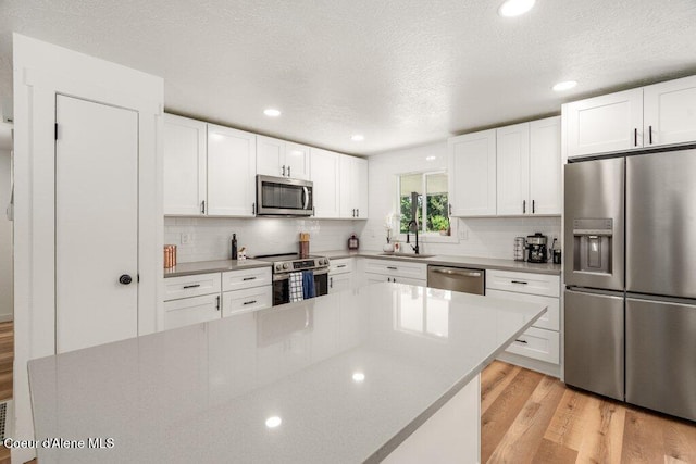 320 E Dakota Ave, Hayden, ID 83835 - kitchen with appliances with stainless steel finishes, light wood-style flooring, decorative backsplash, white cabinets, and light countertops