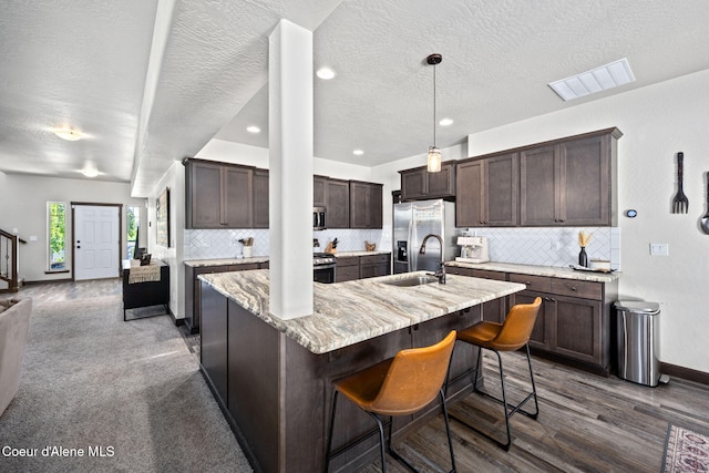2499 N N Side Saddle Ln, Post Falls, ID 83854 - kitchen with stainless steel appliances, dark brown cabinetry, tasteful backsplash, a kitchen island with sink, and a textured ceiling