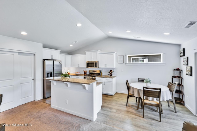 3631 N Britton Rd, Post Falls, ID 83854 - kitchen featuring stainless steel appliances, a kitchen breakfast bar, dark stone counters, white cabinetry, and lofted ceiling
