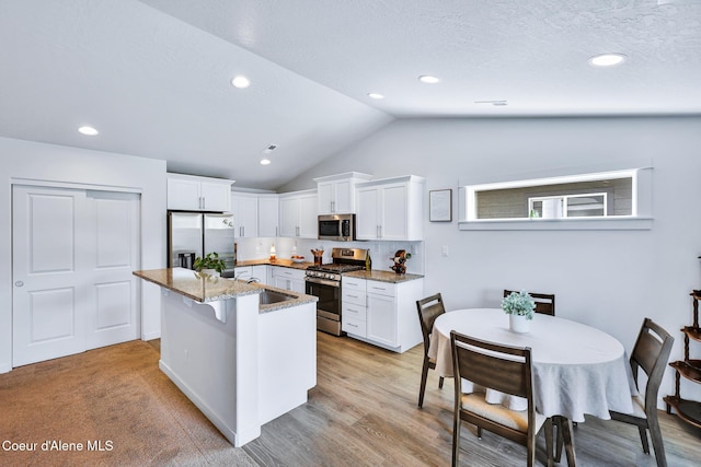 3631 N Britton Rd, Post Falls, ID 83854 - kitchen with stainless steel appliances, vaulted ceiling, white cabinets, light stone countertops, and an island with sink