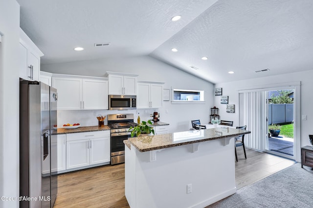 3631 N Britton Rd, Post Falls, ID 83854 - kitchen with stainless steel appliances, vaulted ceiling, dark stone countertops, white cabinetry, and light wood-type flooring