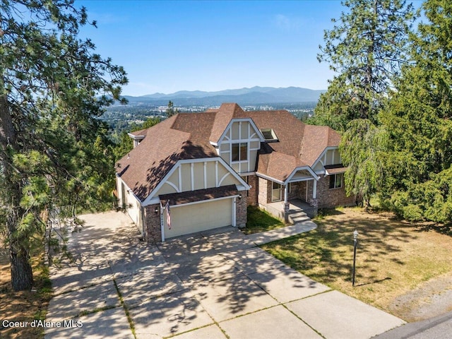 2699 E Packsaddle Dr, Coeur Dalene, ID 83815 - tudor house featuring an attached garage, concrete driveway, roof with shingles, a mountain view, and brick siding