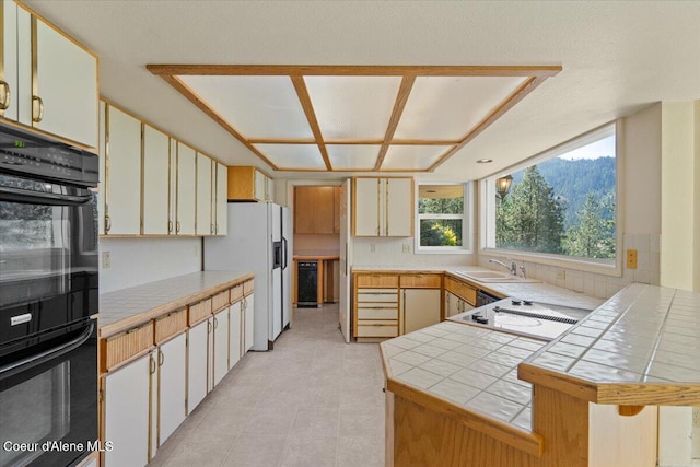 2699 E Packsaddle Dr, Coeur Dalene, ID 83815 - kitchen with tile counters, white fridge with ice dispenser, light tile patterned floors, stovetop with downdraft, and a peninsula