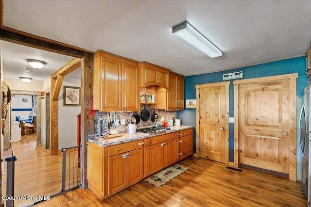 3297 Minaloosa Valley Rd, Plummer, ID 83851 - kitchen with light wood-style flooring, tasteful backsplash, stainless steel gas cooktop, brown cabinets, and light stone countertops