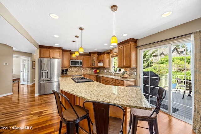5570 E Shoreline Dr, Post Falls, ID 83854 - kitchen featuring appliances with stainless steel finishes, brown cabinetry, tasteful backsplash, light wood finished floors, and light stone counters