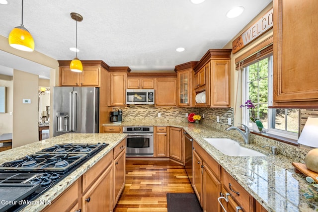 5570 E Shoreline Dr, Post Falls, ID 83854 - kitchen with appliances with stainless steel finishes, brown cabinets, light wood finished floors, decorative light fixtures, and decorative backsplash