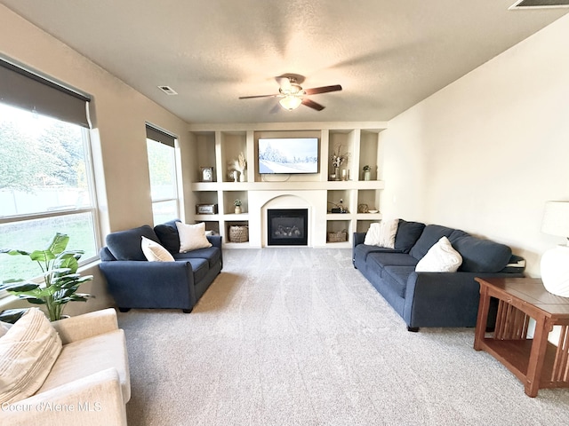 2699 E Thrush Dr, Post Falls, ID 83854 - living room featuring carpet flooring, built in features, a ceiling fan, a glass covered fireplace, and a textured ceiling