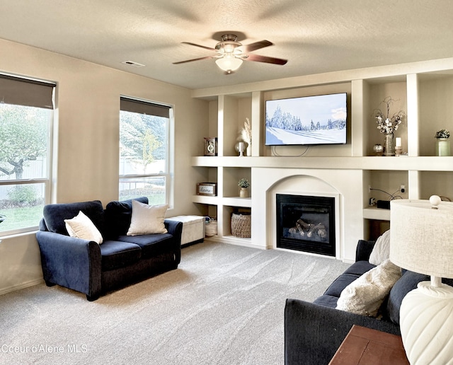 2699 E Thrush Dr, Post Falls, ID 83854 - carpeted living room featuring ceiling fan, a textured ceiling, built in shelves, a glass covered fireplace, and plenty of natural light