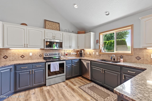2042 W Heavenly Star Ct, Post Falls, ID 83854 - kitchen featuring stainless steel appliances, white cabinets, vaulted ceiling, light stone countertops, and light wood-style floors
