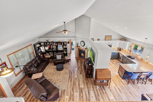 2042 W Heavenly Star Ct, Post Falls, ID 83854 - living room featuring light wood finished floors, a glass covered fireplace, a ceiling fan, a textured ceiling, and high vaulted ceiling
