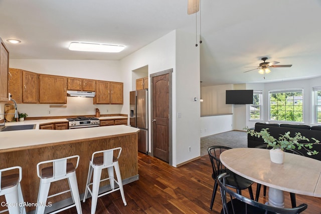 7386 W Sunrise Ct, Rathdrum, ID 83858 - kitchen with under cabinet range hood, stainless steel appliances, ceiling fan, brown cabinetry, and dark wood finished floors