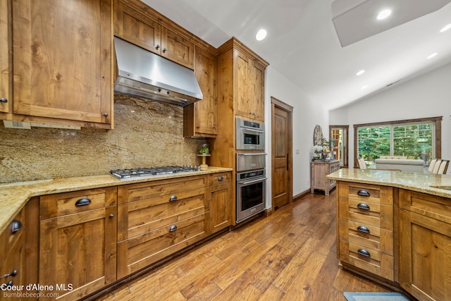 12500 N Partridge Way, Hayden, ID 83835 - kitchen featuring under cabinet range hood, stainless steel gas cooktop, brown cabinetry, tasteful backsplash, and vaulted ceiling