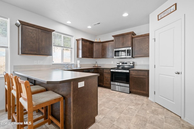 21714 S Lakeview Dr, Worley, ID 83876 - kitchen featuring appliances with stainless steel finishes, dark brown cabinetry, a peninsula, a kitchen breakfast bar, and recessed lighting