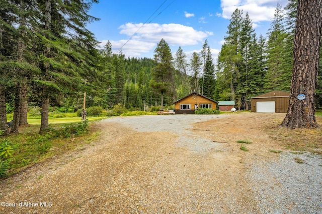 215 Gordon Dr, Priest Lake, ID 83856 - view of front of house featuring a detached garage, an outbuilding, driveway, and a forest view