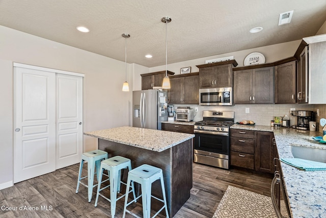 4483 N Connery Loop, Post Falls, ID 83854 - kitchen featuring appliances with stainless steel finishes, dark brown cabinetry, dark wood-type flooring, a center island, and a breakfast bar area