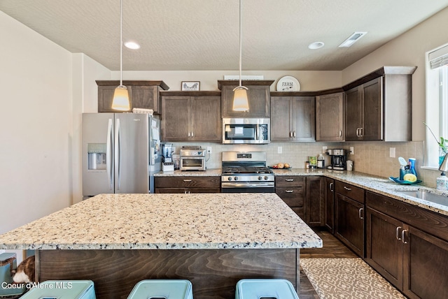4483 N Connery Loop, Post Falls, ID 83854 - kitchen featuring appliances with stainless steel finishes, dark brown cabinetry, light stone counters, tasteful backsplash, and decorative light fixtures