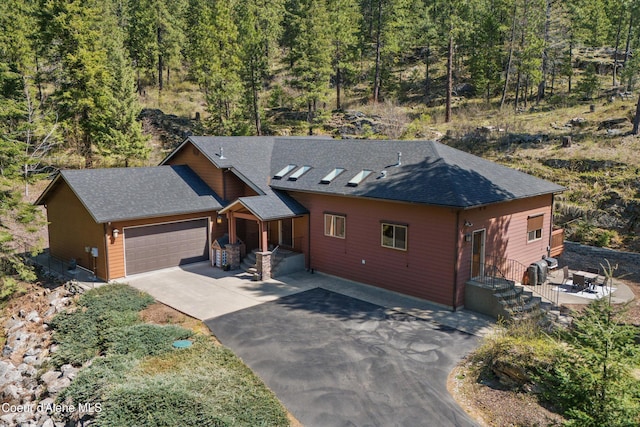 23388 N Teddy Loop, Rathdrum, ID 83858 - chalet / cabin with asphalt driveway, a garage, a shingled roof, and a view of trees