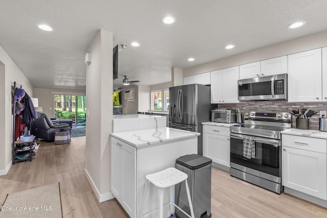5299 W Green Ct # 23, Rathdrum, ID 83858 - kitchen with stainless steel appliances, open floor plan, white cabinets, backsplash, and light wood-style floors