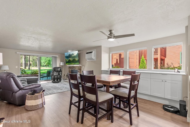 5299 W Green Ct # 23, Rathdrum, ID 83858 - dining space featuring a textured ceiling, light wood-style flooring, a wall mounted AC, a ceiling fan, and a fireplace