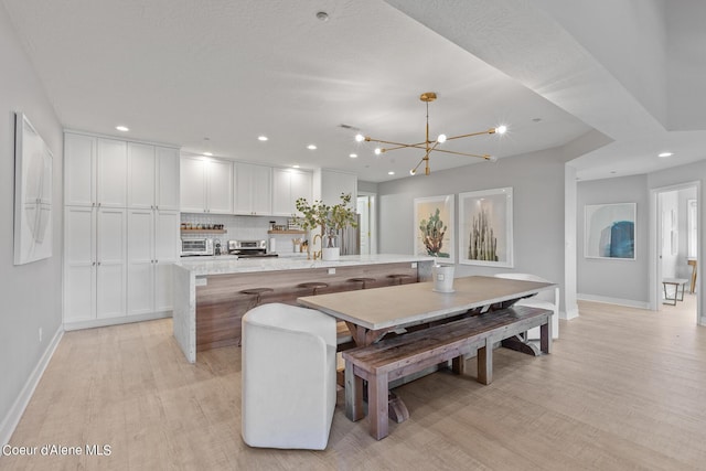 4732 S Arrow Point Dr # 304, Harrison, ID 83833 - kitchen featuring light wood-type flooring, a center island with sink, decorative backsplash, white cabinetry, and recessed lighting