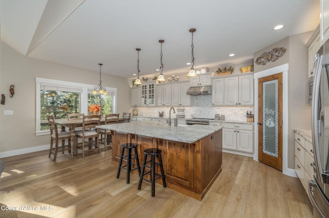 16749 W Cade Rd, Hauser, ID 83854 - kitchen with under cabinet range hood, light wood-type flooring, decorative backsplash, a kitchen breakfast bar, and a center island with sink