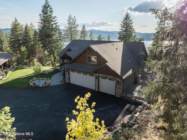 16749 W Cade Rd, Hauser, ID 83854 - view of front of house with asphalt driveway, stone siding, a garage, a front lawn, and a mountain view