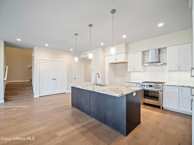 993 E Railroad Ave, Post Falls, ID 83854 - kitchen with wall chimney range hood, high end stove, white cabinetry, light wood-type flooring, and backsplash