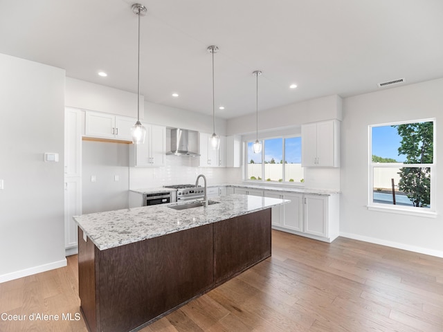 1037 E Railroad Ave, Post Falls, ID 83854 - kitchen featuring wall chimney range hood, white cabinetry, light stone counters, backsplash, and light wood-style floors