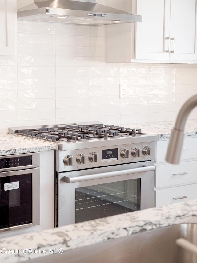 1037 E Railroad Ave, Post Falls, ID 83854 - kitchen with appliances with stainless steel finishes, backsplash, wall chimney exhaust hood, white cabinetry, and light stone countertops
