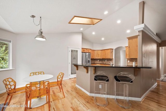 5188 E Twila Ct, Post Falls, ID 83854 - kitchen featuring stainless steel refrigerator with ice dispenser, vaulted ceiling, a peninsula, dark countertops, and a breakfast bar