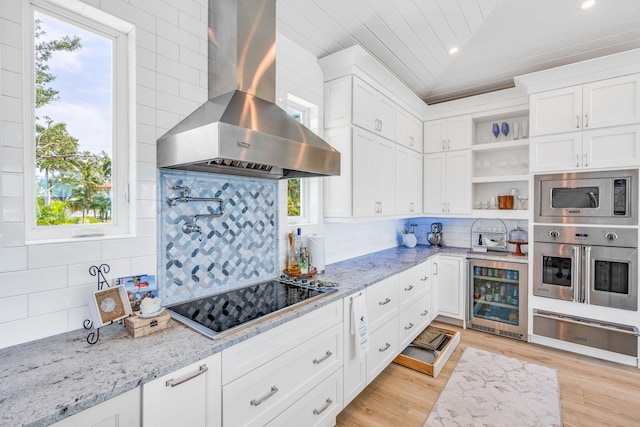 kitchen featuring white cabinetry, wine cooler, light stone counters, black electric cooktop, and wall chimney exhaust hood