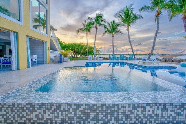 pool at dusk featuring a patio area and a jacuzzi