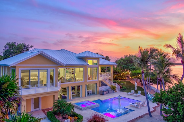 pool at dusk featuring a patio and an in ground hot tub