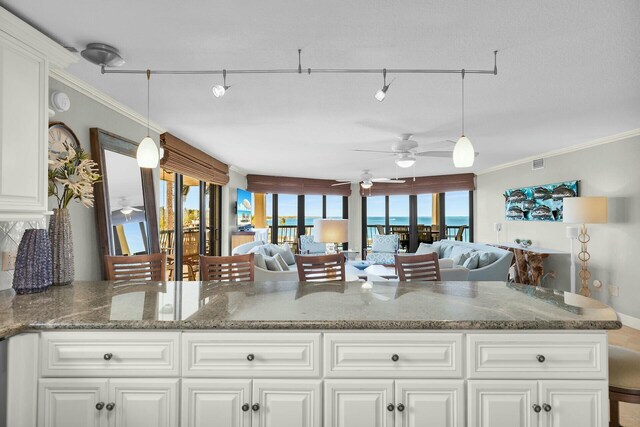 kitchen with stone countertops, ornamental molding, open floor plan, white cabinetry, and hanging light fixtures