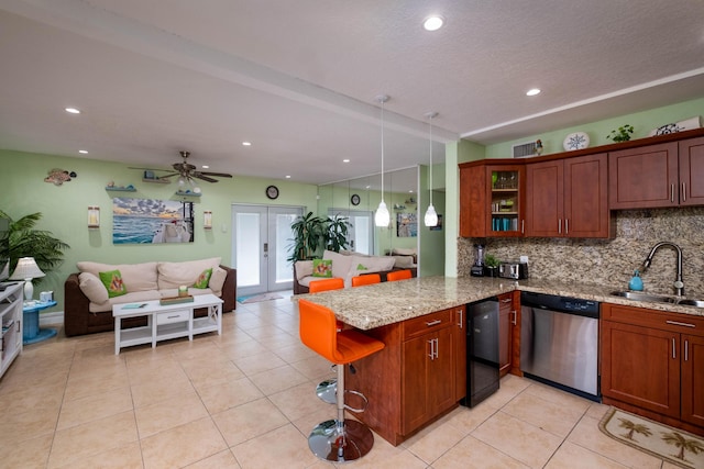 kitchen with light stone countertops, stainless steel dishwasher, backsplash, a sink, and a peninsula