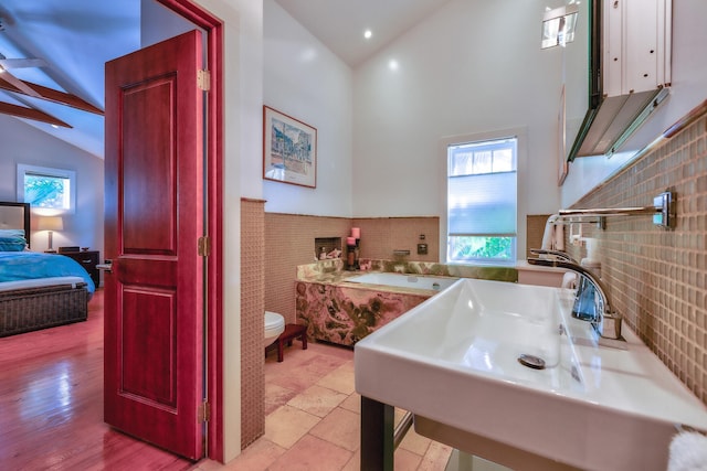 ensuite bathroom featuring tile walls, connected bathroom, wainscoting, toilet, and a sink