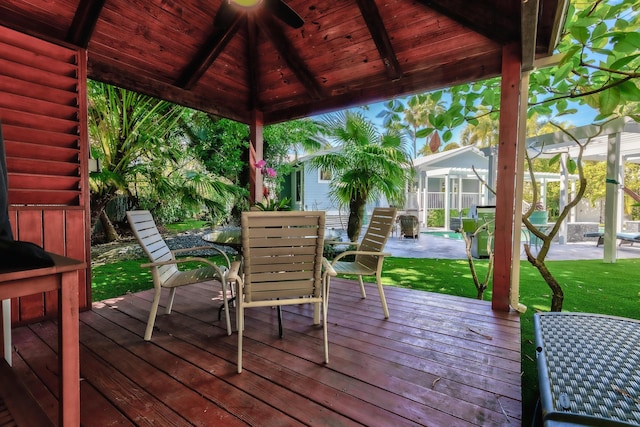 wooden deck with outdoor dining space, glass enclosure, a lawn, and a gazebo