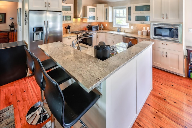 kitchen with wall chimney exhaust hood, appliances with stainless steel finishes, backsplash, and light wood-style flooring