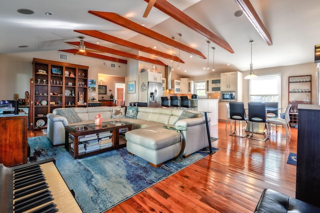 living area featuring light wood-style floors, visible vents, lofted ceiling with beams, and a ceiling fan