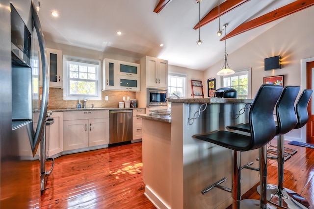 kitchen featuring stainless steel appliances, a breakfast bar, vaulted ceiling with beams, and decorative backsplash