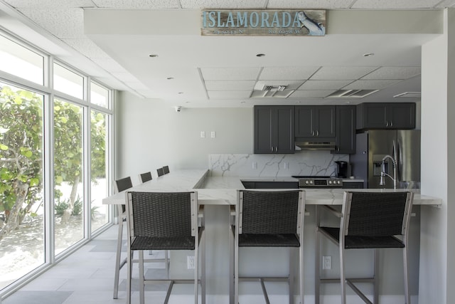 kitchen with light stone counters, stainless steel fridge with ice dispenser, a kitchen breakfast bar, and kitchen peninsula