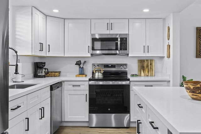 kitchen with sink, hardwood / wood-style flooring, white cabinets, and appliances with stainless steel finishes