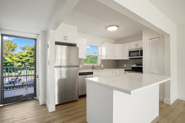 kitchen featuring appliances with stainless steel finishes, light hardwood / wood-style floors, white cabinets, a kitchen island, and decorative backsplash