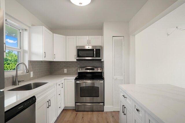 kitchen featuring sink, appliances with stainless steel finishes, backsplash, white cabinets, and light wood-type flooring