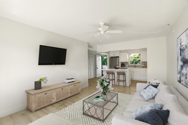 living room featuring ceiling fan, sink, and light hardwood / wood-style floors