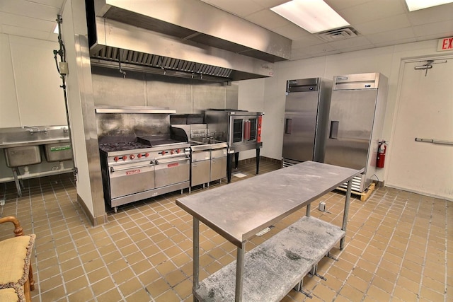 kitchen featuring visible vents, stainless steel refrigerator with ice dispenser, a drop ceiling, stainless steel fridge, and wall chimney exhaust hood