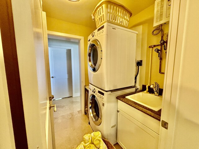 clothes washing area with cabinet space, stacked washing maching and dryer, and a sink