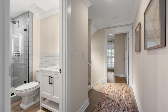 bathroom featuring toilet, wood-type flooring, a tile shower, ornamental molding, and vanity