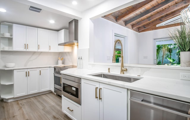 kitchen with wall chimney exhaust hood, appliances with stainless steel finishes, sink, and white cabinets